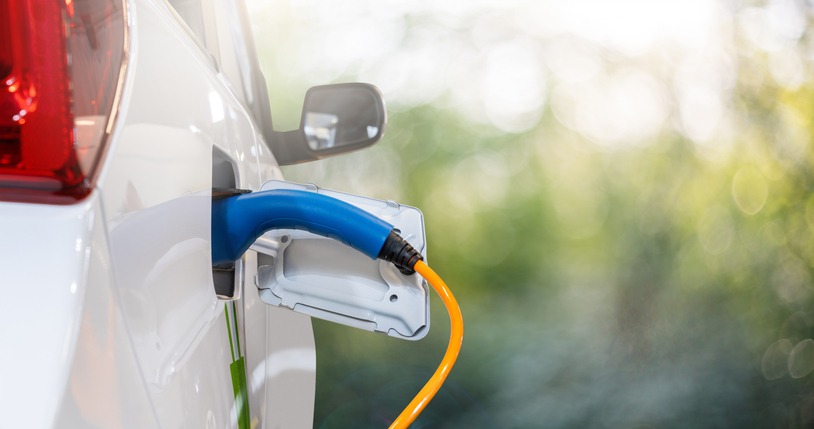 Nahaufnahme des Elektroauto-Einlasses mit angeschlossenem Ladekabel auf grünem Hintergrund